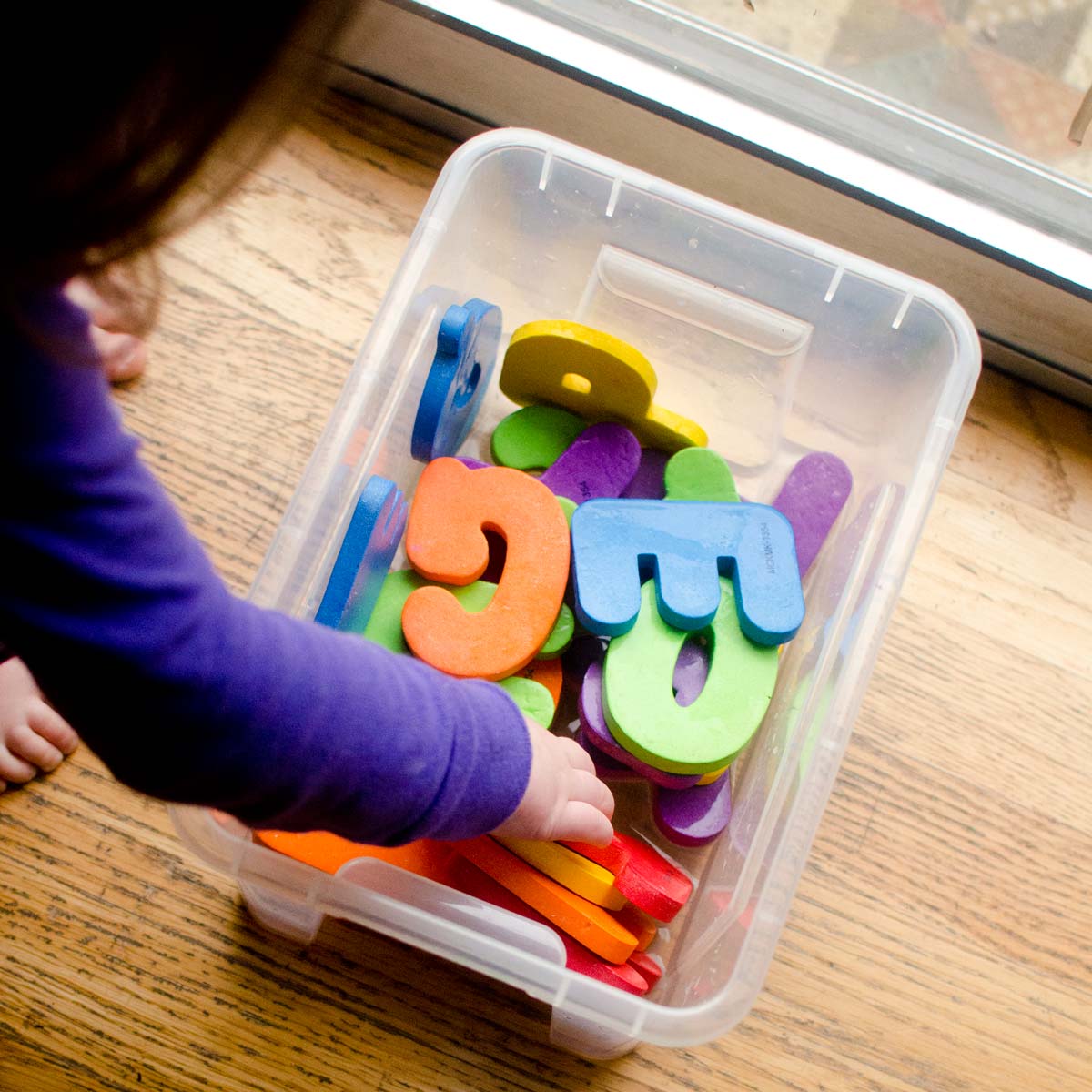 A child reaches into a plastic container full of water and foam alphabet letters.