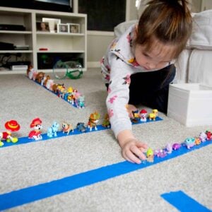 A child leans over a line of painter's tape to delicately place a small toy animal into a line-up