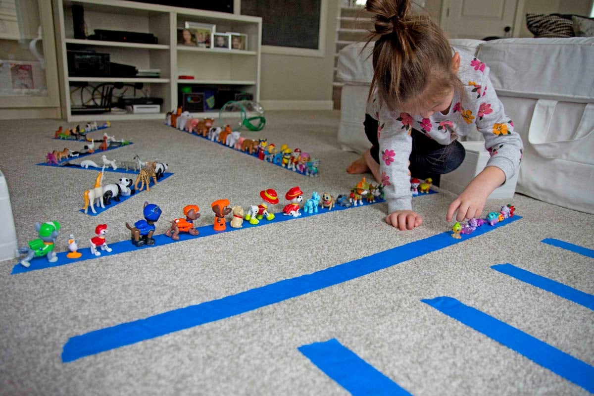 A child places Hatchimal toys onto a strip of blue tape. There are more animals on tape strips behind her.