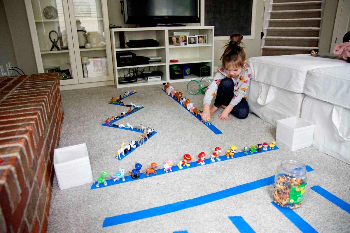 A child places animal toys onto strips of blue tape in her family room.