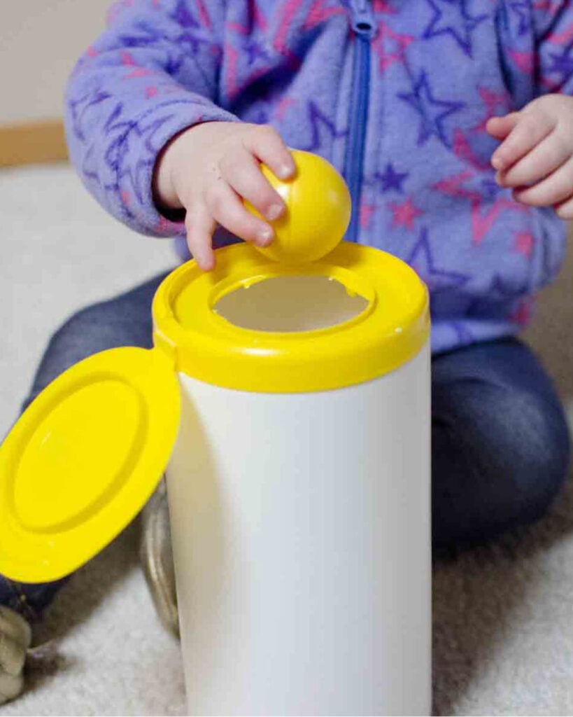 A child drops balls into a wipes container.