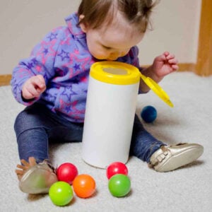 A baby looks into a wipes container for the ball she dropped
