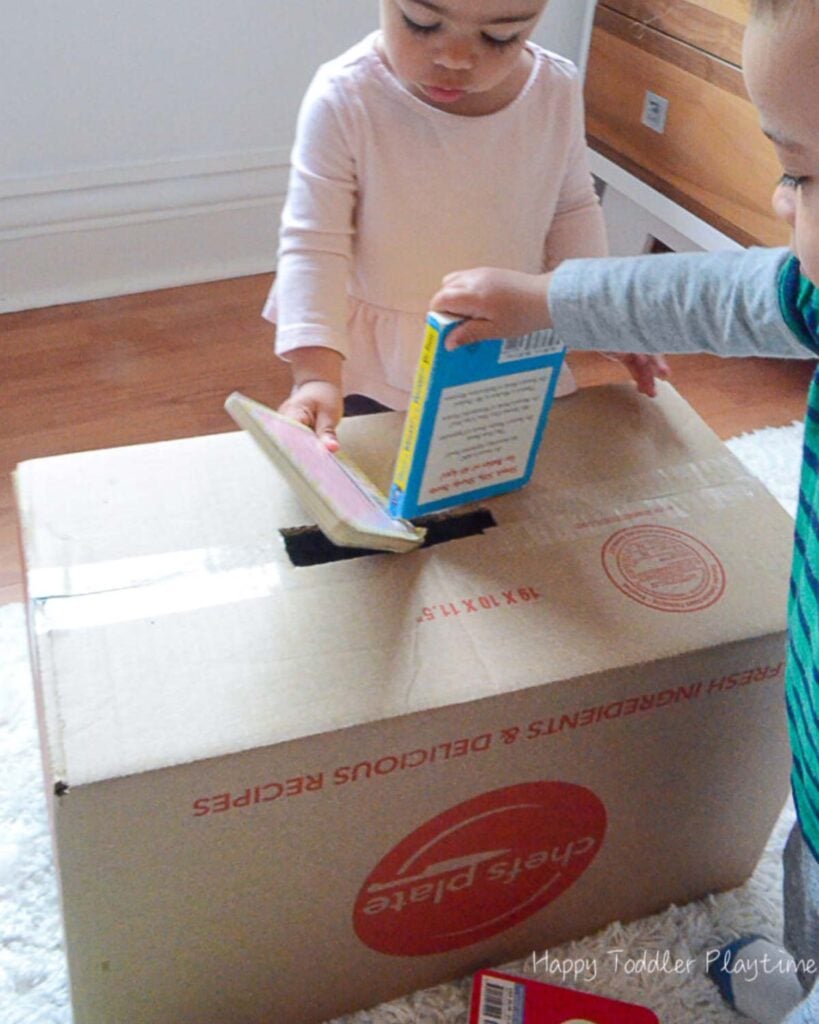 Two kids push books into a box.
