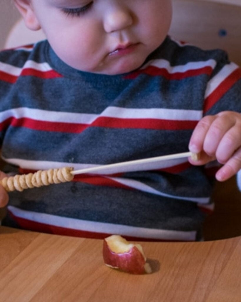 Child threads cheerios on a stick
