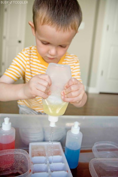 Kid playing at a colored water mixing station using peri bottles to hold the liquid from Busy Toddler
