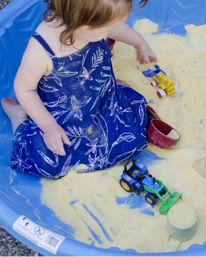 A child plays in a kiddie pool full of cornmeal.
