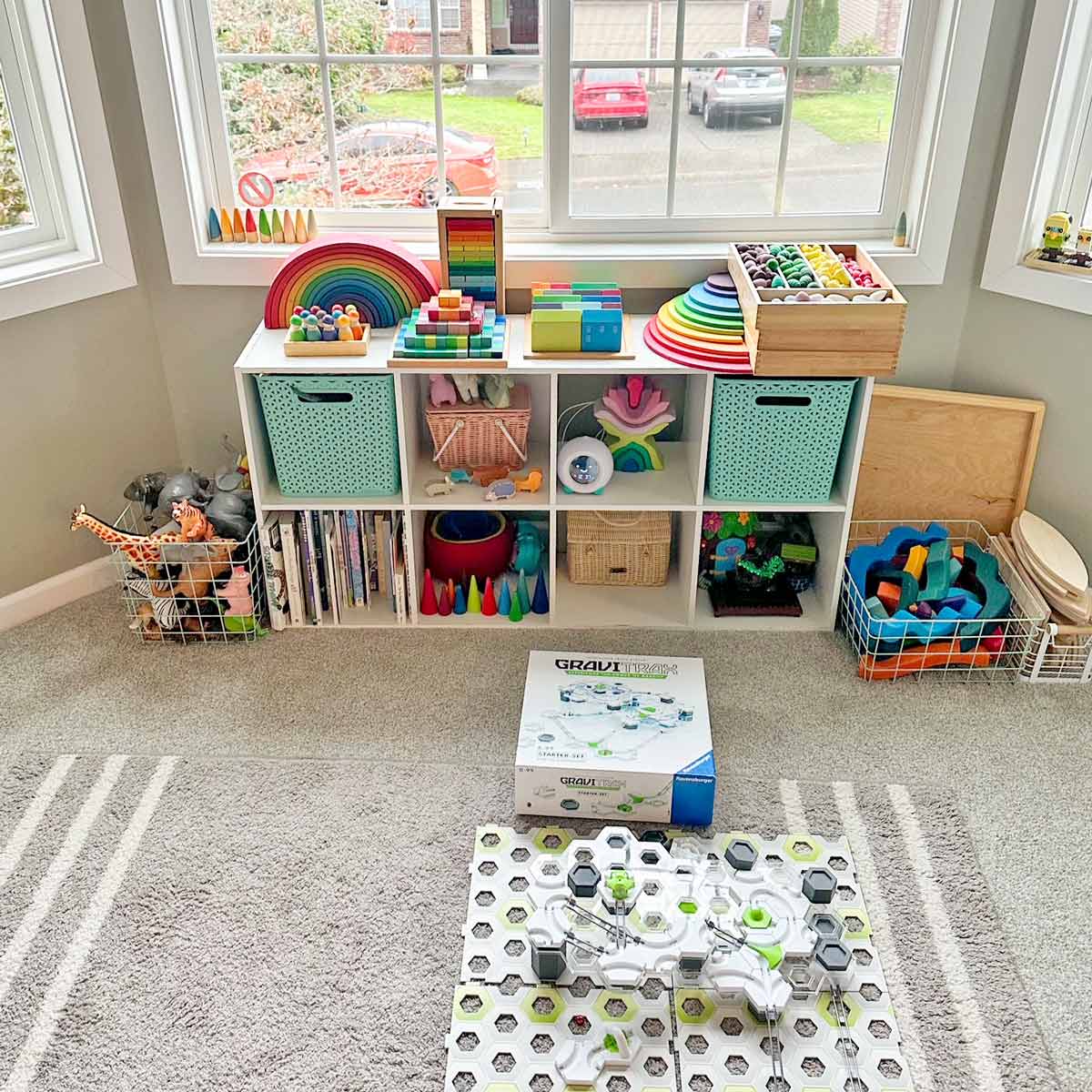 A child's bookshelf is pictured full of toys organized in plastic and win bins and baskets.