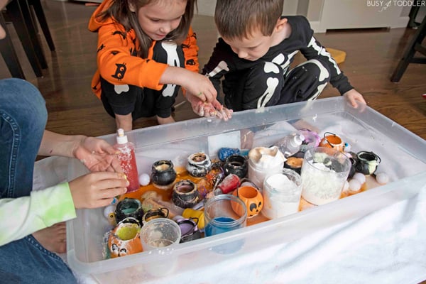 A science sensory bin with three kids working on potions. Corn starch covers varies concuctions. 