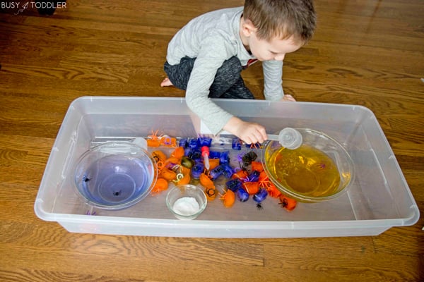 Child playing with ice cubes and plastic spiders in a Halloween science activity