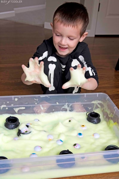 A child playing with green bubble foam has his hands covered. 