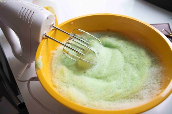 Halloween bubble foam being made in a yellow bowl with a hand mixer