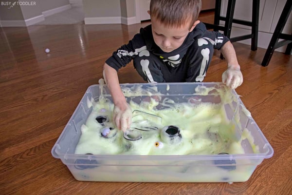 A child playing with green bubble foam in a Halloween themed sensory bin.
