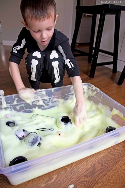 A child gasps while playing with a Halloween themed sensory bin made of green bubble foam