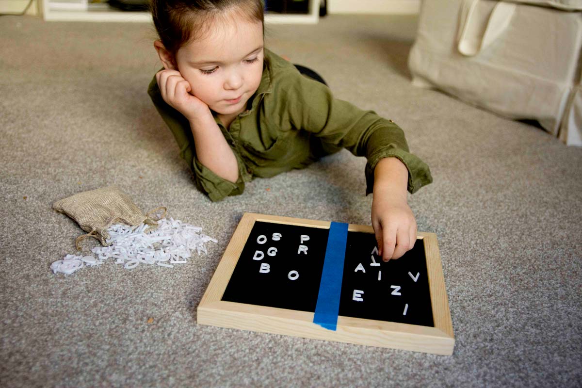 A child places a letter onto a letter board. The letter board has blue tape down the middle dividing it into two sections.