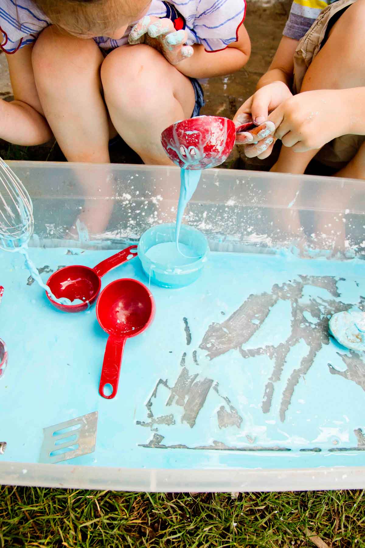 A child drips oobleck from a measuring cup into a blue bowl.