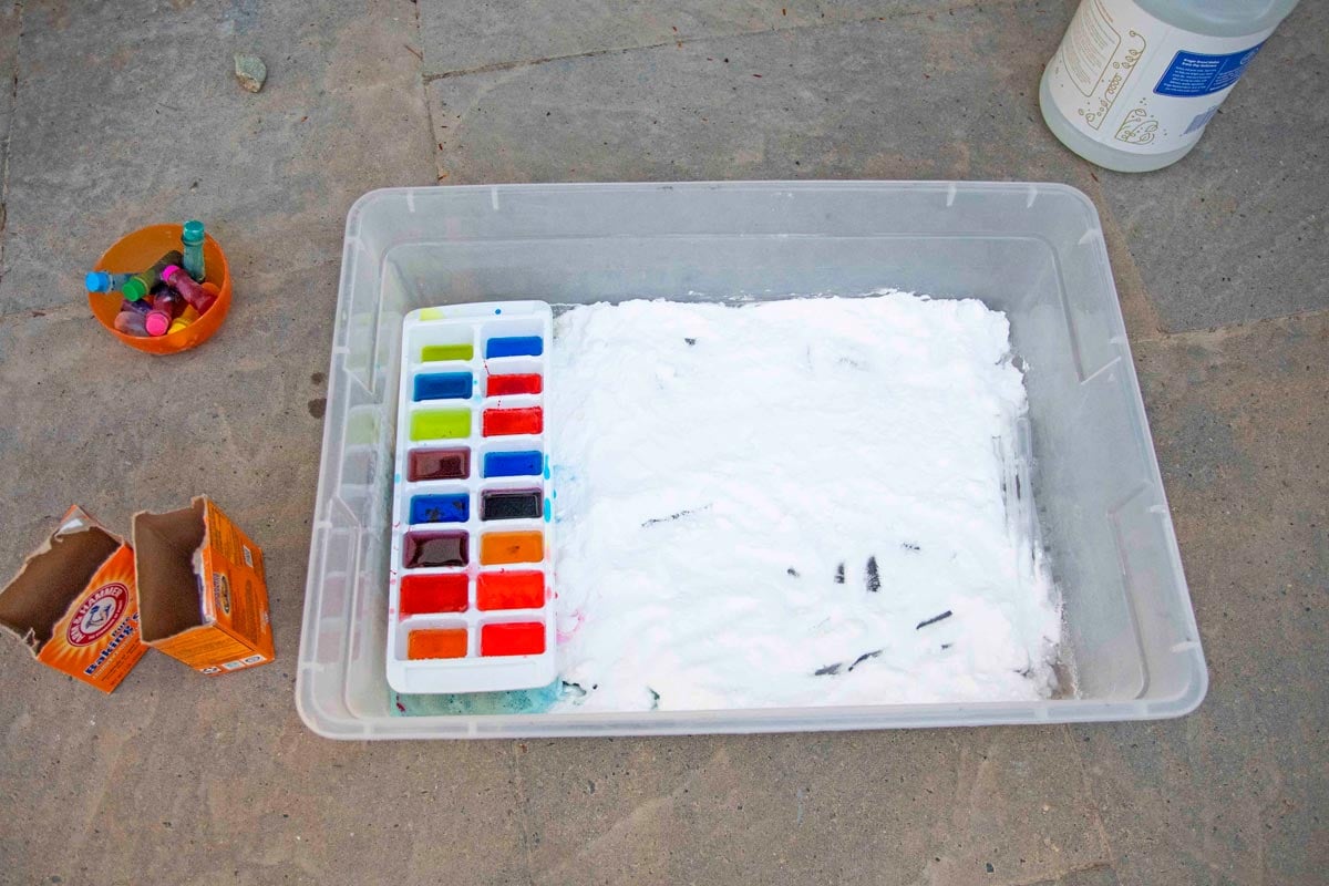 A bin full of baking soda with a colorful ice cube tray of vinegar inside.