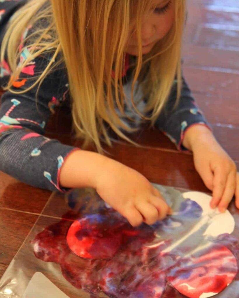 A child paints flowers in a plastic bag.