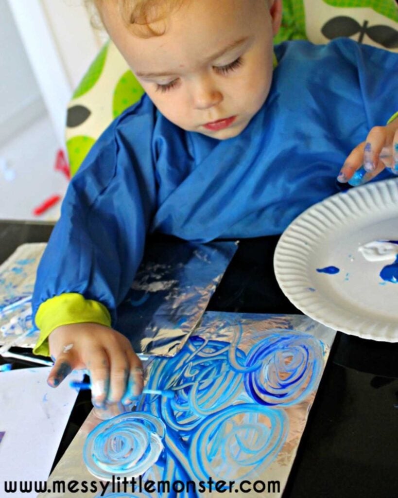 A child uses cotton swabs to paint on foil.