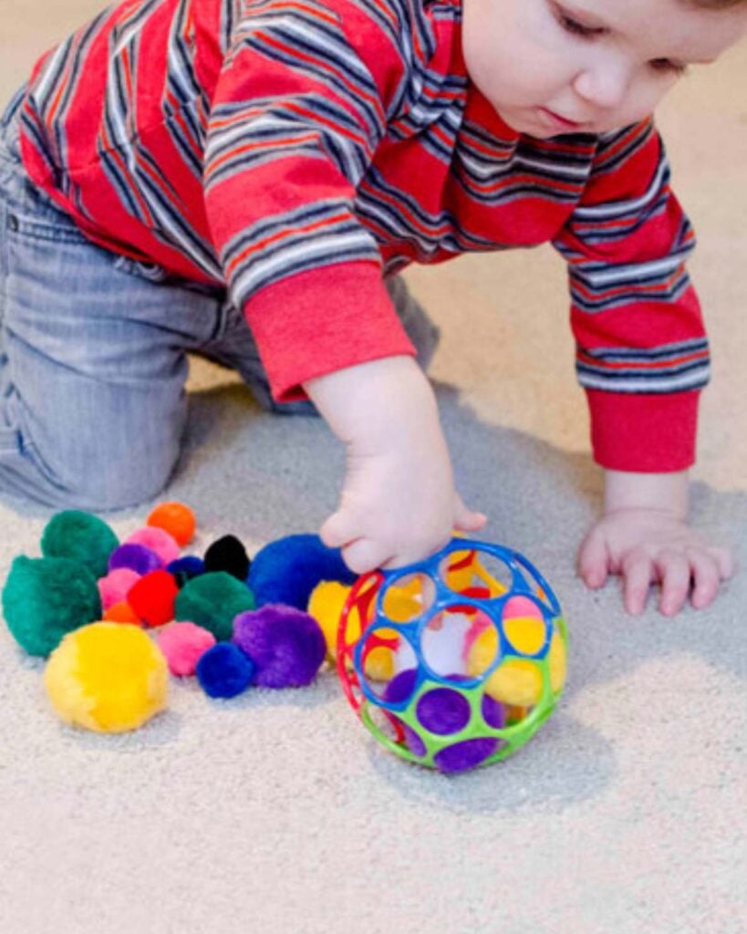 A child pushes a pom pom ball into a Oball
