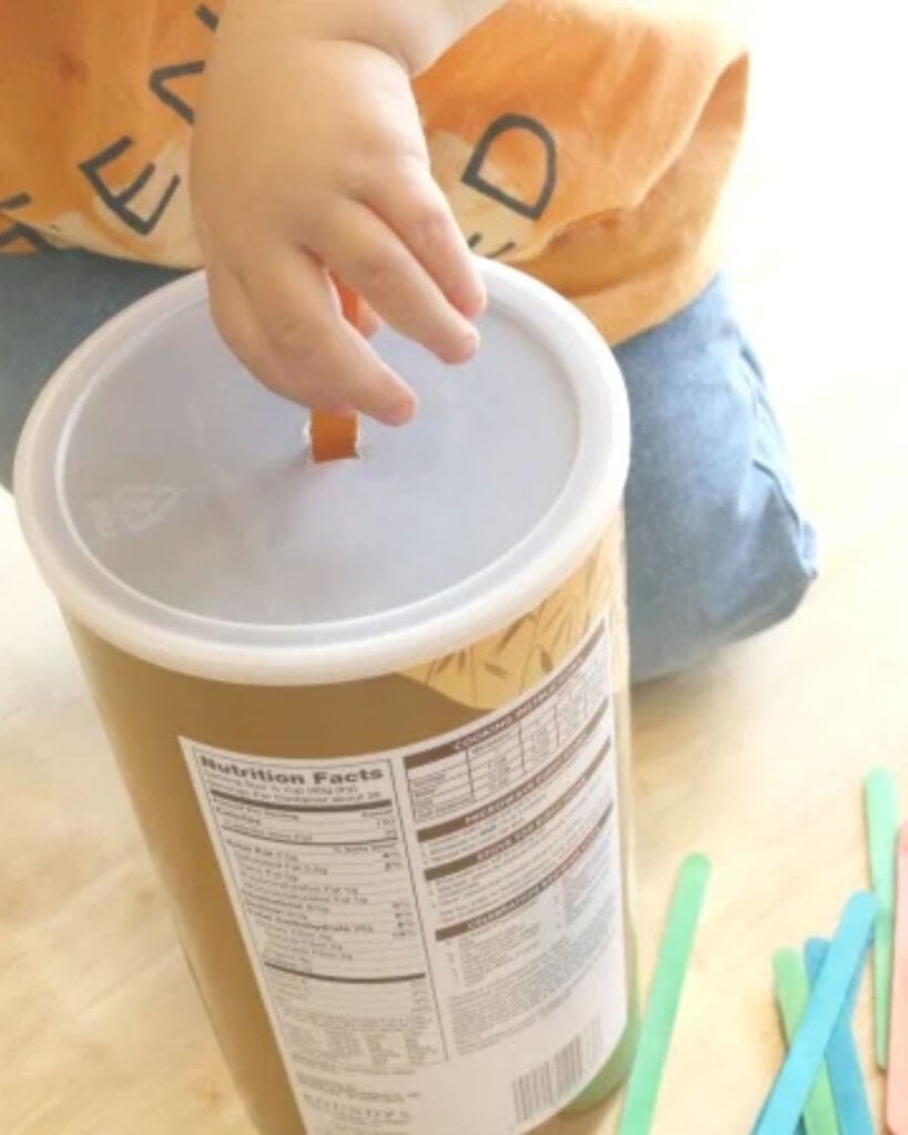 A child pushes a Popsicle stick into an oats container.