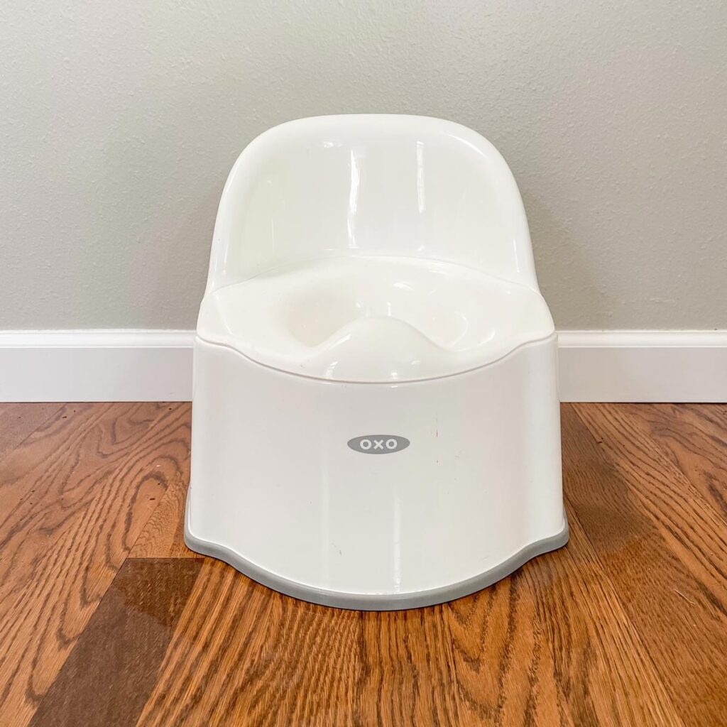A child's toilet on a hardwood floor with gray walls behind it.