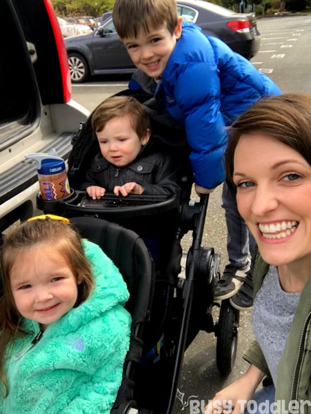 A parent takes a selfie of three kids on a stroller.