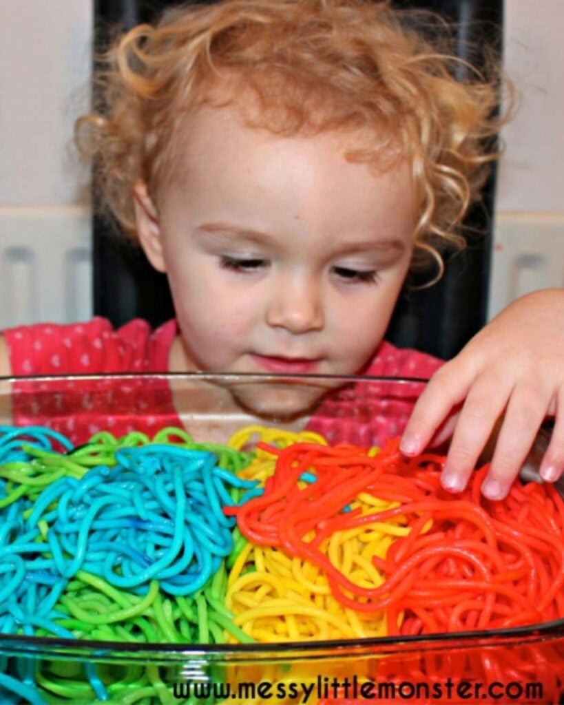 A child looks at a bowl of rainbow dyed spaghetti.