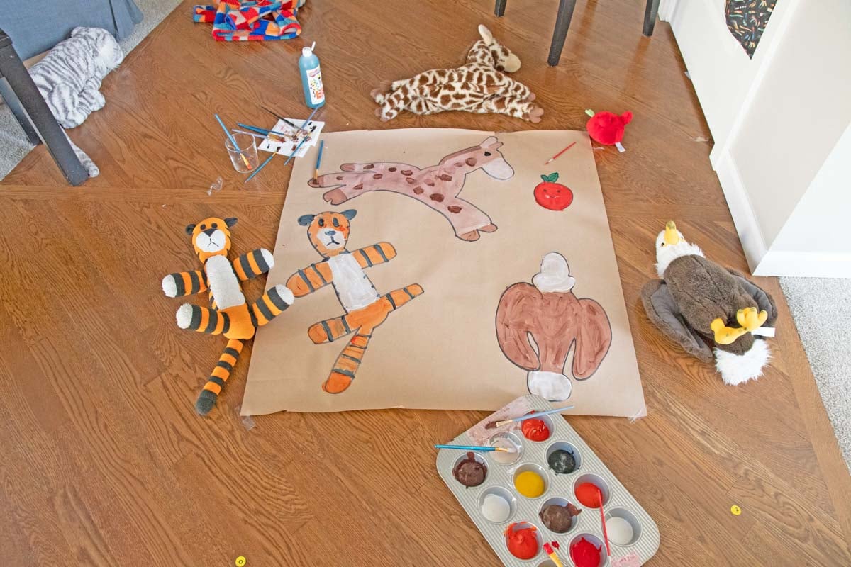 The final product of kids painting pictures of their stuffed animals: a giraffe, Hobbes, apple, and eagle stuffed toys are all redrawn on paper.