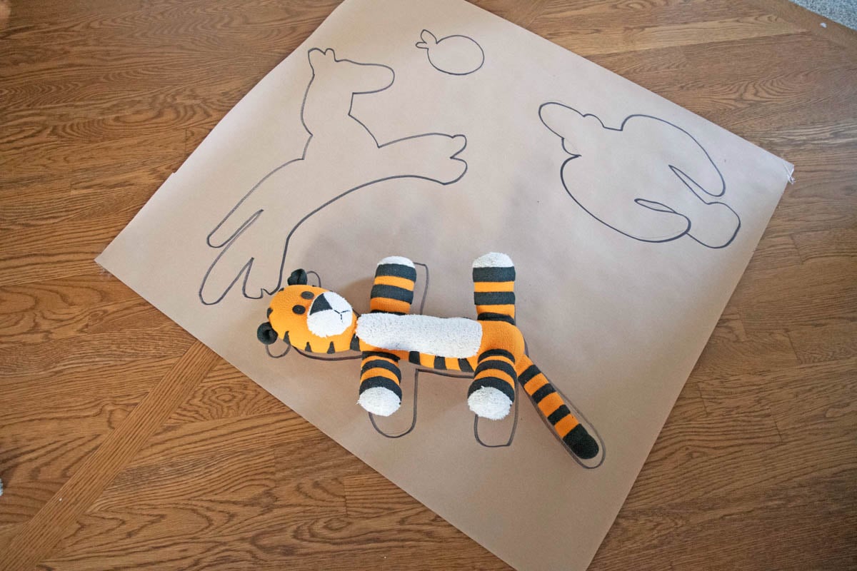 A brown piece of paper has outlines of stuffed animals drawn on it and a Hobbes stuffed animal, too.