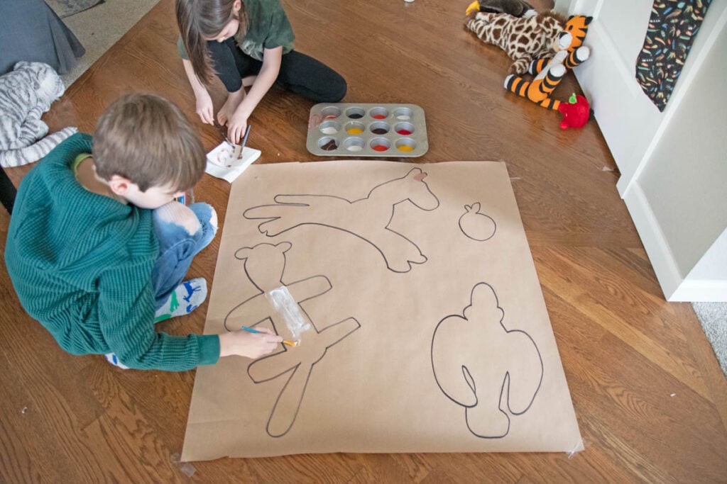 Two kids paint outlines of their stuffed animals on paper.
