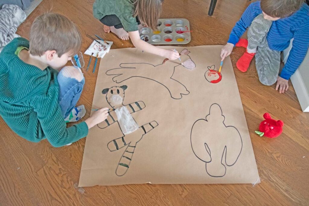 Three kids paint outlines of their stuffed animals on paper.