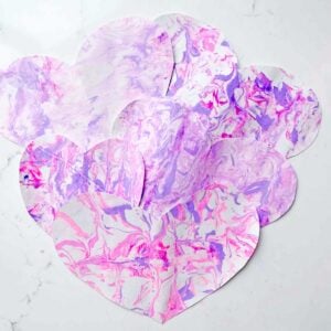 A set of shaving cream marble hearts sits on a white countertop. The marble pattern is made of purples and pinks.