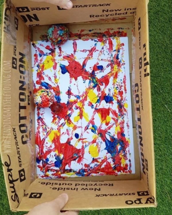 A child rolls balls in a box with paint
