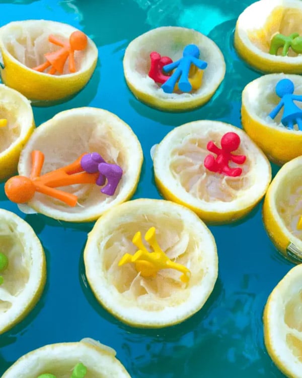 Cut up lemons with small toys float in a water sensory bin.