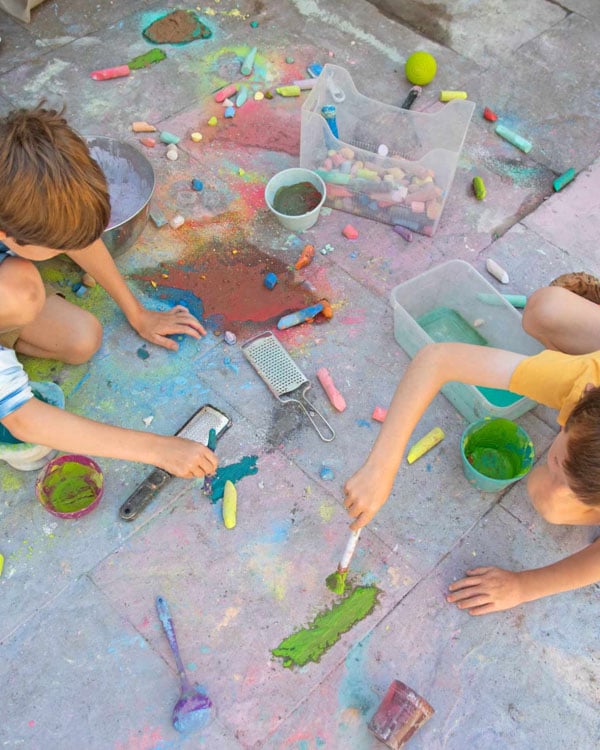 Two children work with chalk paint on a patio.