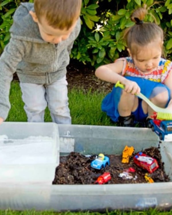 Two children play at a water and mud sensory bin cleaning dirty cars.