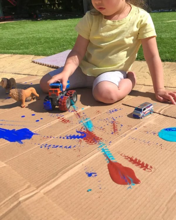 A child rolls cars throw paint to make track prints.
