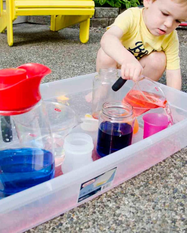 A child pours water into a sensory bin pouring station.