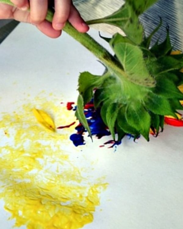 A child uses flowers dipped in paint to paint on white paper