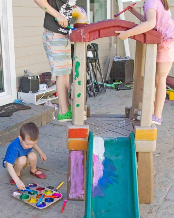 Three kids paint on a plastic playhouse. They are painting the actual play house.