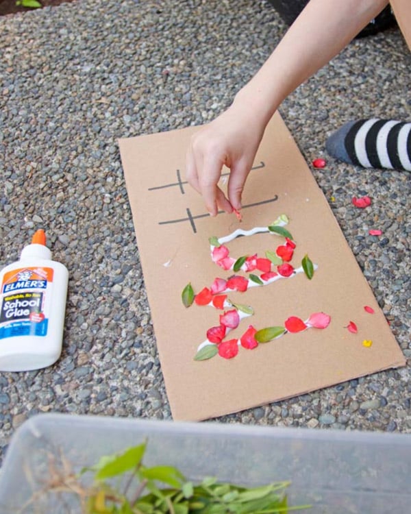 A child places petals onto cardboard to spell their name.