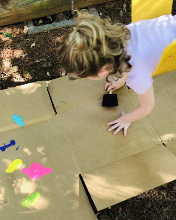 A child on a swing paints on cardboard below her.