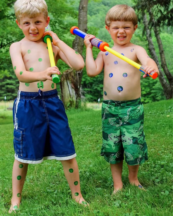 Two children with paint on their bellies play with water blasters.